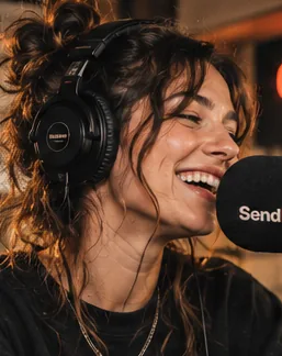 A radio maker wearing headphones laughs at the microphone.